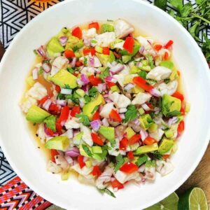 White fish ceviche with avocado, red onion, red pepper, and cilantro in a white bowl, overhead.