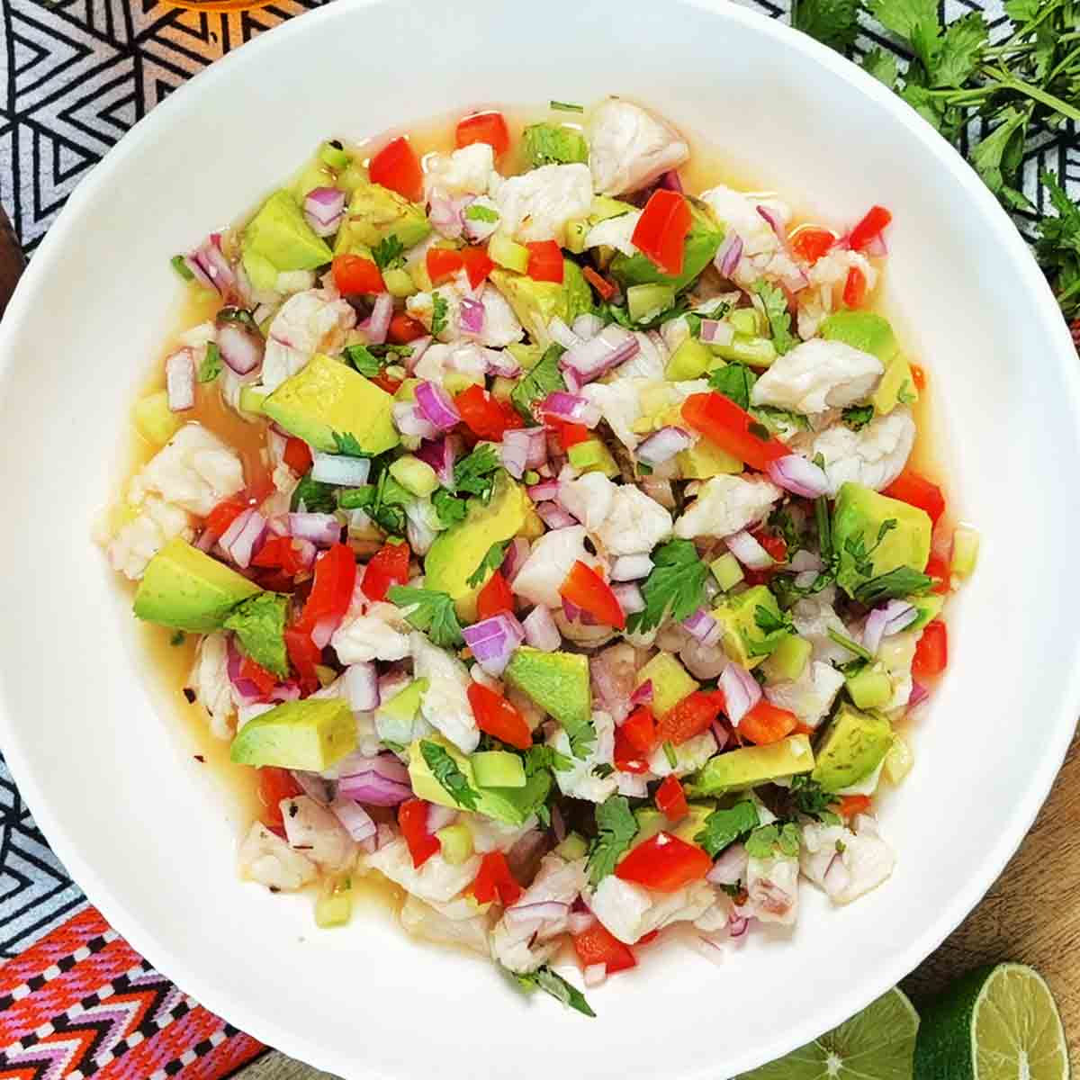 White fish ceviche with avocado, red onion, red pepper, and cilantro in a white bowl, overhead.